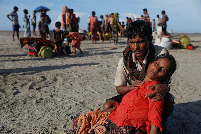 ၂၀၁၇ အောက်တိုဘာလက မြန်မာစစ်တပ်၏နှိမ်နင်းမှုကြောင့် မြန်မာနိုင်ငံမှသစ်သားလှေဖြင့်ဘင်္ဂလားဒေ့ရှ် သို့ထွက်ပြေးရောက်ရှိစဉ် ပင်ပန်းလွန်း၍ပျော့ခွေလဲကျနေသောဇနီးသည် ရှာကီရာကို အာရစ်ဖ်အူလာ က နှစ်သိမ့်ပေးနေပုံ (ရိုက်တာ/ဒါမီယာဆာဂိုလ်ဂျ်)