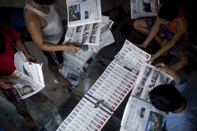 ရန်ကုန် ပုံနှိပ်စက်ရုံတစ်ခုရှိ အလုပ်သမားများက နေ့စဉ်ထုတ် သတင်းများအား စီစစ်နေသည်ကို  တွေ့ရစဉ်။ (ဓာတ်ပုံ - AFP)